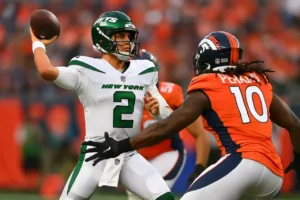 Rozgrywający New York Jets unika presji obrońcy Denver Broncos podczas meczu NFL 2025 – dynamiczna akcja na boisku futbolowym.